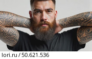 Brutal attractive bearded biker man with tattooed hands poses in black blank t-shirt from premium thin cotton, isolated on white mockup. Стоковое AI-видео, аниматор Sergey Grishin / Фотобанк Лори