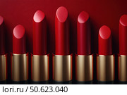 Row of passion red lipsticks displayed against a vibrant red background. Beauty industry and fashion concept. Copy space. Advertisement for makeup artists. Стоковое AI-изображение, AI-художник Ирина Михайличенко / Фотобанк Лори