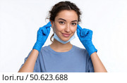 Young woman wearing blue nitrile gloves putting on protective face mask. Стоковое AI-изображение, AI-художник Юрий Поздников / Фотобанк Лори