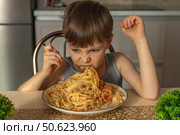 Happy boy eating tasty pasta at table in kitchen. Стоковое фото, фотограф Михаил Яковлев / Фотобанк Лори