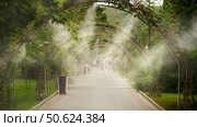 Outdoor air cooling system (fogging) in extreme heat. Spraying moisture over the road with pedestrians in the distance. Стоковое фото, фотограф Роман Дзюбало / Фотобанк Лори
