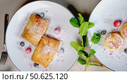 Traditional Ukrainian breakfast featuring syrniki and nalysnyky with fresh berries, mint garnish, powdered sugar sprinkled on white ceramic plates, silverware nearby. Стоковое видео, видеограф Данил Руденко / Фотобанк Лори