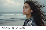 Closeup shot of pretty teenage girl with long dark curly hair wearing casual cozy plaid shirt, staying alone, thinking, dreaming, watching at camera, catching wind in her haircut. Стоковое AI-видео, аниматор Sergey Grishin / Фотобанк Лори
