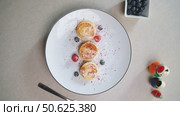 Eastern European syrniki cheese pancakes plated with mixed berries, dusted with powdered sugar, fork alongside crisp white ceramic surface. Стоковое видео, видеограф Данил Руденко / Фотобанк Лори