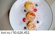 Syrniki cheese pancakes spinning gently, dusted with powdered sugar, adorned with fresh berries on pristine white ceramic plate against neutral background. Стоковое видео, видеограф Данил Руденко / Фотобанк Лори