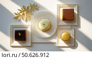 Elegant gourmet desserts in geometric shapes displayed with golden leaves and luxury presentation on white table under soft sunlight, emphasizing fine patisserie art. Стоковое AI-изображение, AI-художник Катерина Бондарец / Фотобанк Лори