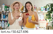 Smiling young female friends scanning bottles of sunscreen and tanning lotion in personal care store using phone, checking ingredients while choosing best option for safe and glowing summer tan. Стоковое видео, видеограф Яков Филимонов / Фотобанк Лори