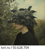 A surreal portrait of a young woman in profile against a natural backdrop. She is wearing a black lace dress and an unusual headdress made of thick leaves with black birds sitting in them. The atmosphere of the image is mysterious and mystical, with hints of Gothic and symbolism. Soft diffused light and muted colors create a sense of sleep, mystery, and merging with nature. Стоковое AI-изображение, AI-художник Анна Кривицкая / Фотобанк Лори