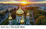 Aerial view of a beautiful Orthodox cathedral with golden domes, overlooking a city skyline at a dramatic sunset. Стоковое AI-видео, аниматор Sergey Grishin / Фотобанк Лори