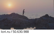 An Asian man fishing from a cliff in the sea against the background of the setting sun. He's twisting a reel of fishing line, but he hasn't caught anything. Стоковое видео, видеограф Владимир Разгуляев / Фотобанк Лори