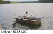 A young man is paddling a boat next to a pier in the middle of the river in summer. Стоковое видео, видеограф Strunov David / Фотобанк Лори