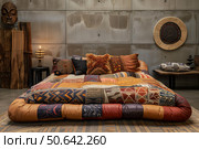 Comfortable futon bed with ethnic pillows and blankets in modern interior design. Стоковое AI-изображение, AI-художник Иван Рябоконь / Фотобанк Лори