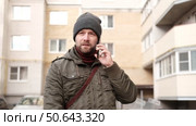 Handsome man wearing warm jacket and wool hat walking down on the city with mobile phone in hand. Stylish bearded middle-aged male using smartphone at urban street. Businessman going on job. Стоковое видео, видеограф Марина Демидюк / Фотобанк Лори