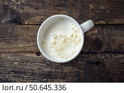 Frothy milk resting in white mug on rustic wooden table. Стоковое AI-изображение, AI-художник Иван Рябоконь / Фотобанк Лори
