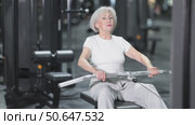 In gym, senior woman uses cable row machine to strengthen arm muscles. Стоковое видео, видеограф Яков Филимонов / Фотобанк Лори
