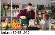 Seller weighs tangerines in a bag for a boy. Child buys fruit in the supermarket. Fresh citrus fruits in the grocery store. Стоковое видео, видеограф Яков Филимонов / Фотобанк Лори