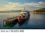 Ferry docking at pier on calm sea at sunset with island in background. Стоковое AI-изображение, AI-художник Иван Рябоконь / Фотобанк Лори
