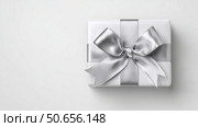 Elegant silver bow adorns a neatly wrapped white gift box on smooth surface. Стоковое AI-изображение, AI-художник Katsiaryna Repich / Фотобанк Лори