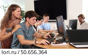 Girl stands behind sitting students, looks at monitor and helps in execution of programing teamwork. Стоковое видео, видеограф Яков Филимонов / Фотобанк Лори