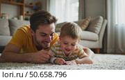 Happy young father lying on floor in living room hold fly with little preschooler son engaged in funny game together, loving dad relax playing with small boy child, enjoy family weekend. Стоковое AI-видео, аниматор Sergey Grishin / Фотобанк Лори