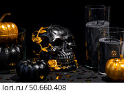 Halloween celebration. Black skull with golden roses, pumpkins, and black candles. Decor for the Day of the Dead or Halloween on a black background. Стоковое фото, фотограф Photojuli / Фотобанк Лори