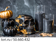 Halloween celebration. Black skull with golden roses, pumpkins, and black candles. Decor for the Day of the Dead or Halloween on a black background. Стоковое фото, фотограф Photojuli / Фотобанк Лори
