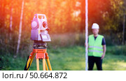 Surveyor engineer topographer with leveling rail on background of forest and tool for geodetic work. Total station and topographer cadastral engineer when performing cadastral work for land surveying. Стоковое фото, фотограф Скрипачев Антон / Фотобанк Лори