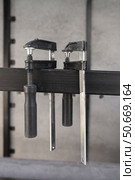 Two clamps for securely holding materials in close up view hang from a metal crossbar on a construction site. Стоковое фото, фотограф Неведицына Елена / Фотобанк Лори