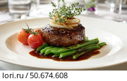 Gourmet beef steak served with green beans, cherry tomatoes, caramelized onions, and herb garnish on elegant white plate in fine dining setting. Стоковое AI-изображение, AI-художник Катерина Бондарец / Фотобанк Лори