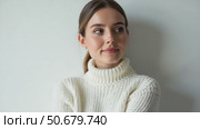 A Young Woman Wearing a Warm White Sweater Looks Thoughtfully at the Camera, Standing Against a Soft Gray Wall. Стоковое AI-видео, аниматор Sergey Grishin / Фотобанк Лори