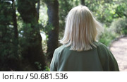 Blonde walking in the park. Happy young woman wearing. Happy young woman in a green jacket walks forward in the park, rear view, slow motion. Стоковое видео, видеограф svetograph / Фотобанк Лори