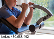 Gym. The picture shows a young man exercising his arms using a pull-up machine. Sports and a healthy lifestyle. Стоковое фото, фотограф Photojuli / Фотобанк Лори