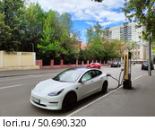 Белый электромобиль Tesla заряжается на улице. Москва (2024 год). Редакционное фото, фотограф Ирина Терентьева / Фотобанк Лори