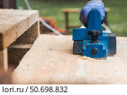 A hand-held electric planer in the hands of a craftsman. A man planing boards with an electric tool. Production of wooden products. Construction, wood processing. Стоковое фото, фотограф Photojuli / Фотобанк Лори