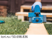 A hand-held electric planer in the hands of a craftsman. A man planing boards with an electric tool. Production of wooden products. Construction, wood processing. Стоковое фото, фотограф Photojuli / Фотобанк Лори