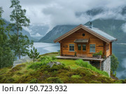 Cozy wooden cabin overlooking scenic norwegian fjord landscape. Стоковое AI-изображение, AI-художник Иван Рябоконь / Фотобанк Лори