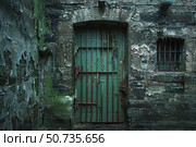 Old rusty green prison door and barred window crumbling stone wall. Стоковое AI-изображение, AI-художник Иван Рябоконь / Фотобанк Лори