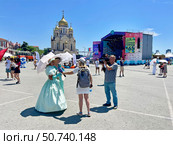 Журналист телеканала берет интервью у женщины в платье, стилизованном под начало 20 века, на площади Борцов Революции в июле 2025 года в День города Владивостока. Редакционное фото, фотограф Овчинникова Ирина / Фотобанк Лори