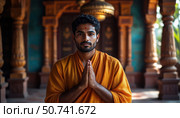 A man in a yellow robe is praying in front of a blue wall. Стоковое AI-изображение, AI-художник Ярославский Максим / Фотобанк Лори