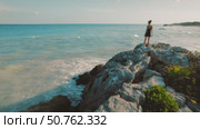 Woman in black dress stands alone on rocky point looking out over calm ocean small waves and sandy seabed in Tulum, Mexico. Стоковое видео, видеограф Igor Tichonow / Фотобанк Лори