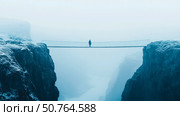 Solitary Figure on a Misty Suspension Bridge Spanning a Deep Gorge. Стоковое AI-изображение, AI-художник Данила Большаков / Фотобанк Лори