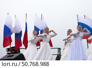 ANGARSK, IRKUTSK REGION, RUSSIA - July 13, 2025: Group of girls in white dresses dance a Buryat folk dance against backdrop of Russian flags. XV International Silk Way Rally. Start of racing competition. Редакционное фото, фотограф Виктория Катьянова / Фотобанк Лори