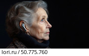 Elderly woman in profile wearing a modern hearing aid, looking thoughtfully ahead against a dark background, symbolizing aging, technology and independence. Стоковое AI-изображение, AI-художник Катерина Бондарец / Фотобанк Лори