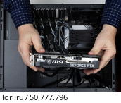 Maykop, Russia - February 18, 2025: Man assembling computer, holding new msi geforce rtx graphics card over asus motherboard in system unit. Редакционное фото, фотограф Андрей С / Фотобанк Лори