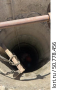 A man with a bucket and a construction helmet at the bottom of a mine shaft. Wooden ladder for well entrance. Mine shaft cleaning. Vertical video. Стоковое видео, видеограф Vadzim Yakubovich / Фотобанк Лори