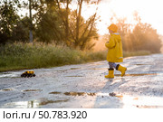 A boy in yellow rubber boots and a raincoat runs through puddles, having fun and playing with a remote-controlled car after it rains. Summer and autumn holidays. A happy childhood. Стоковое фото, фотограф Photojuli / Фотобанк Лори