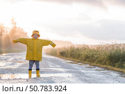 A boy in yellow rubber boots and a raincoat runs through puddles, having fun and playing after it rains. Summer and autumn holidays. A happy childhood. Стоковое фото, фотограф Photojuli / Фотобанк Лори