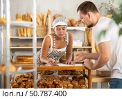 In bakery, male visitor and female salesperson work with paper documents and count using phone. Стоковое фото, фотограф Яков Филимонов / Фотобанк Лори