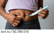 Person holding an injector near abdomen, preparing for self-injection. Cropped view of hands and torso wearing a light top and dark pants. Focus on medical procedure, concept of healthcare. Стоковое AI-изображение, AI-художник Журавлева Кристина / Фотобанк Лори