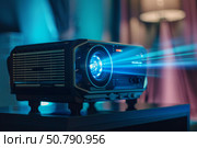 Modern projector projecting bright blue light in cozy living room. Стоковое AI-изображение, AI-художник Иван Рябоконь / Фотобанк Лори